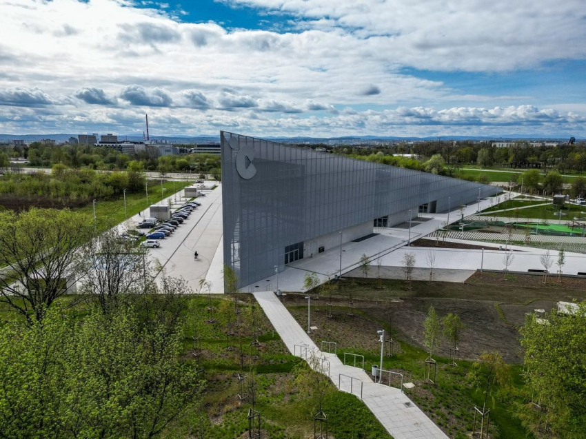 Nowoczesny budynek Centrum Nauki Cogiteon. Przed budynkiem parking samochodowy. Wokół budynku park.