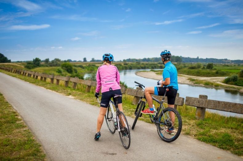 Dwoje rowerzystów, którzy przystanęli na ścieżce rowerowej i patrzą na nadrzeczny krajobraz