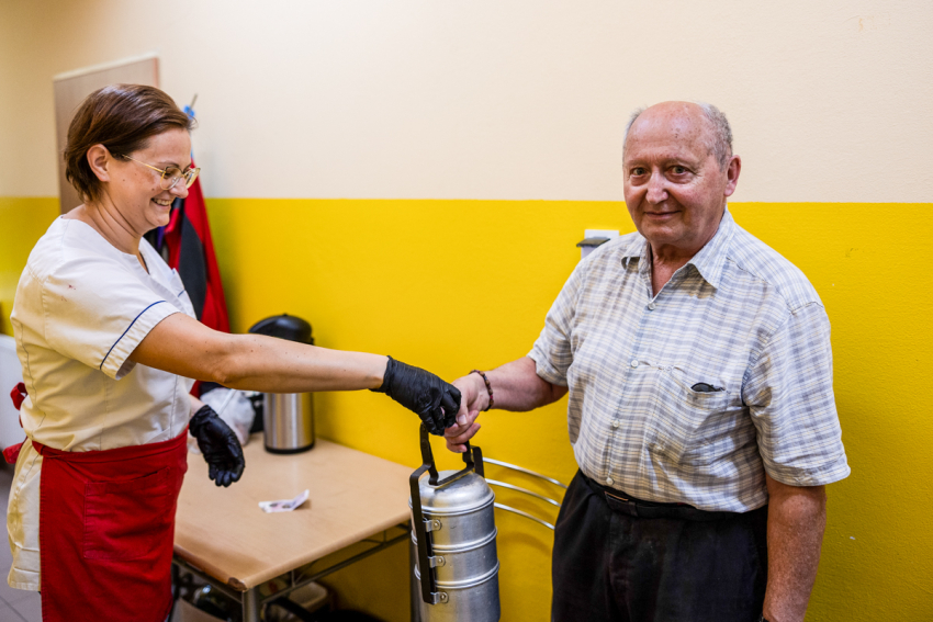 Senior odbiera ciepły posiłek od pani z kuchni.