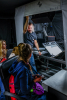 Młody mężczyzna w pracowni digitalizacji pokazuje kilku osobom sprzęt do digitalizacji.