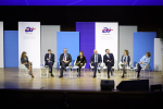 Osiem osób siedzących na krzesłach ustawionych obok siebie na scenie. W głębi kolorowe plasze z logotypem Polskiej prezydencji w Unii Eropejskiej w 2025 roku oraz adresem strony internetowej Poland25.EU